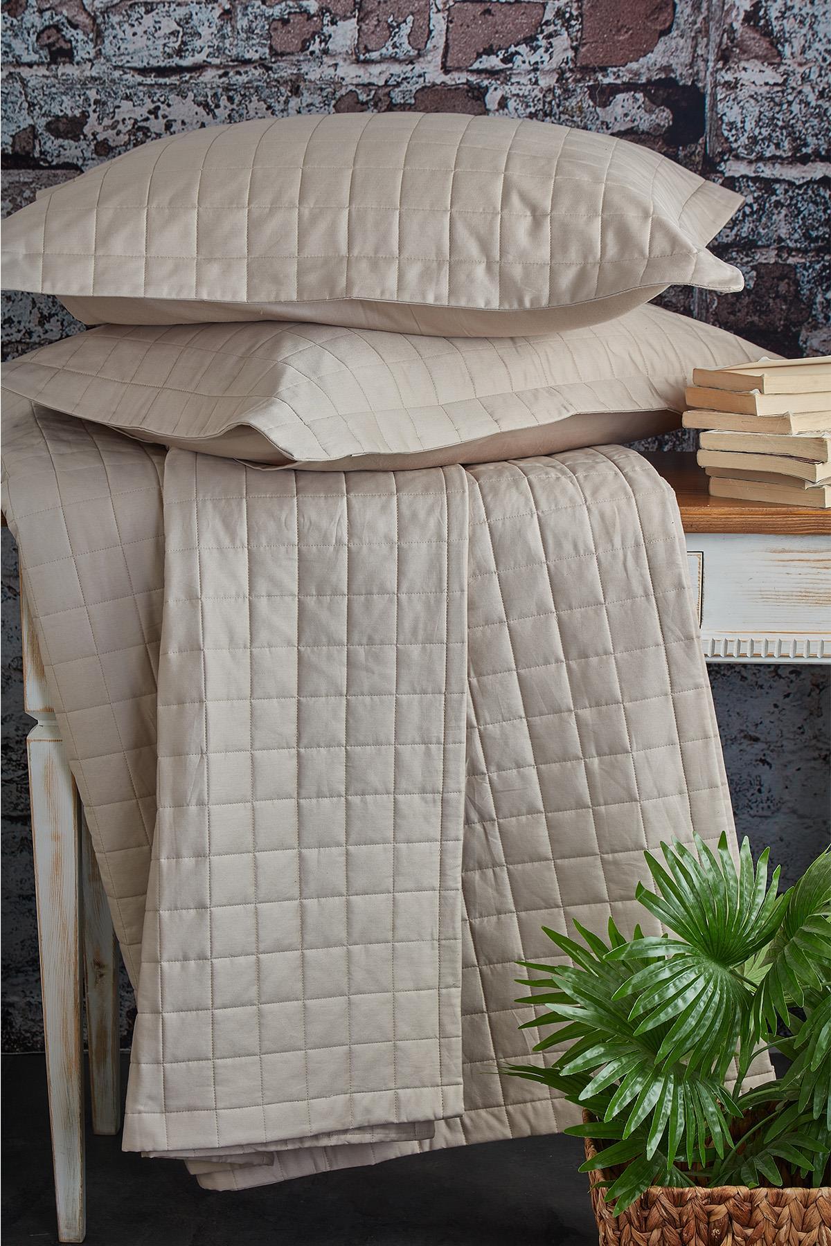 Gesteppte Tagesdecke für Doppelbett, cremefarben, mit zwei Kissen, auf einem Tisch präsentiert