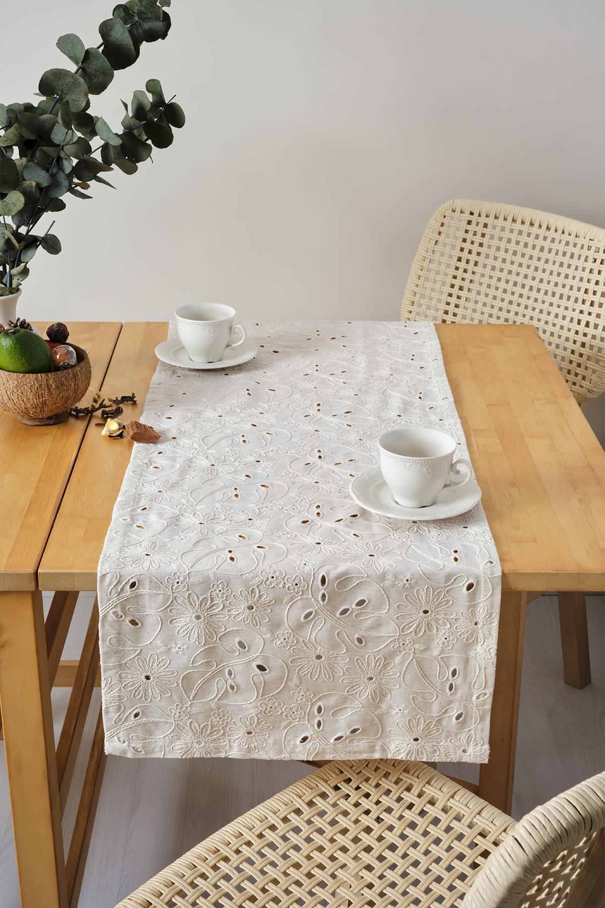 Cremefarbener Tischläufer mit Spitzenstickerei, dekorativ präsentiert auf einem Holztisch mit zwei Tassen