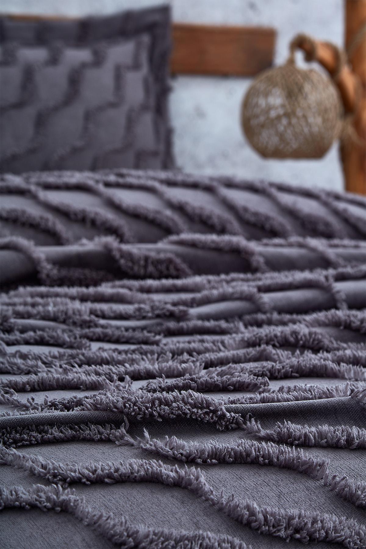 Nahaufnahme einer lilafarbenen Tagesdecke in Leinenoptik für ein Einzelbett mit passendem Kissen.