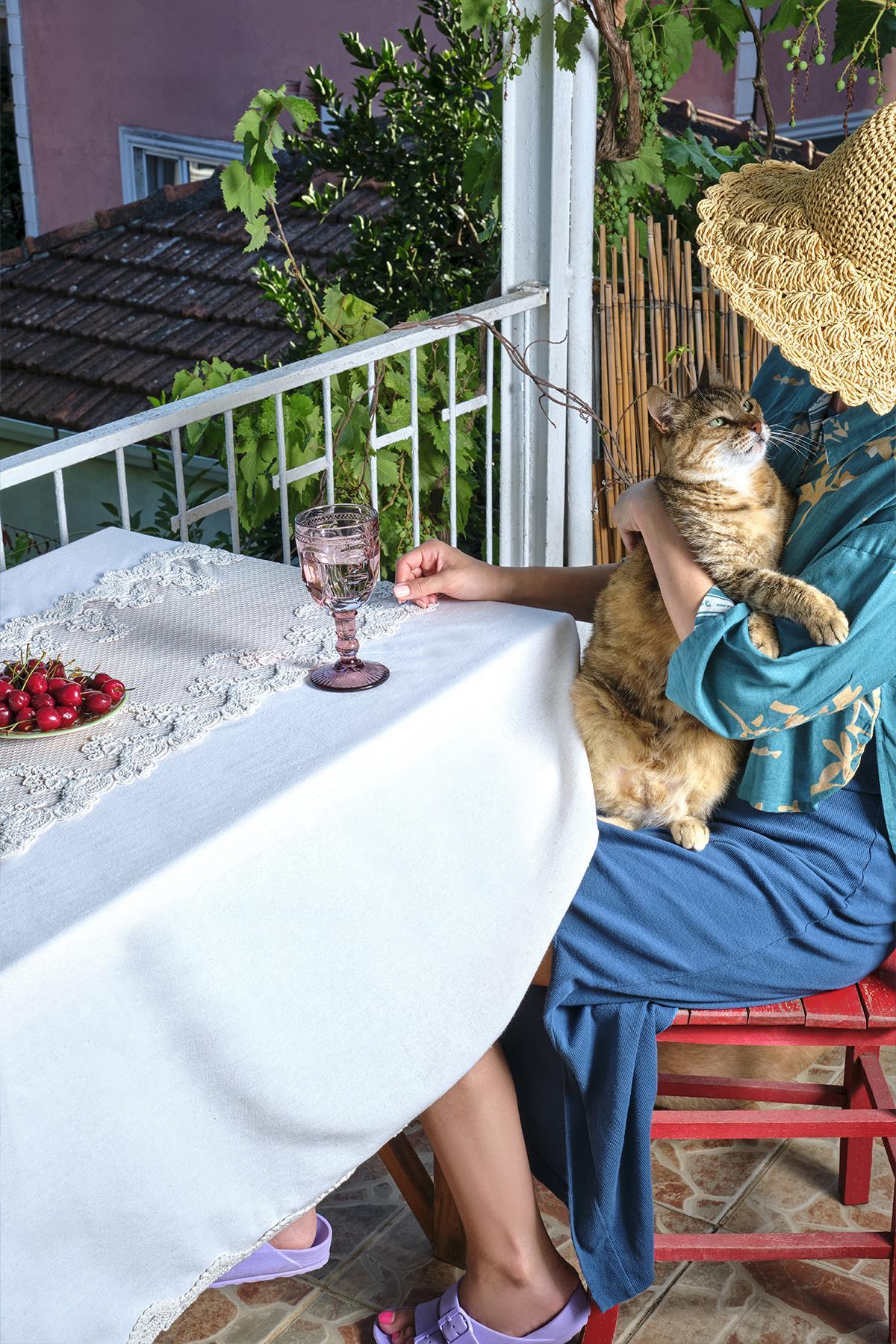 Spitzentischdecke auf einem Balkontisch mit Kirschen, einem rosa Glas und einer Katze daneben