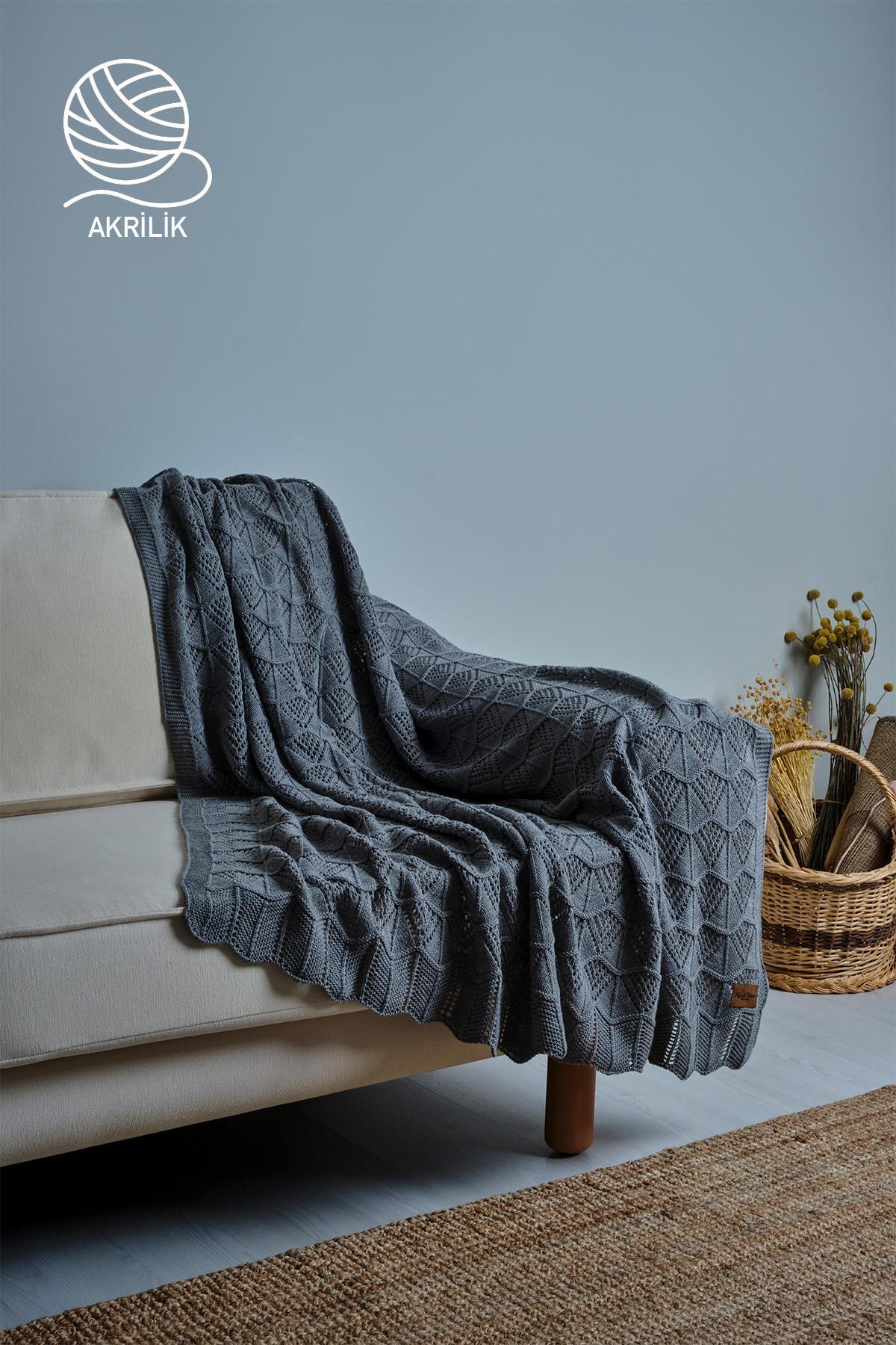 Graue, grob gestrickte TV-Decke aus Acryl, über ein Sofa drapiert, in einem Wohnzimmer-Ambiente.