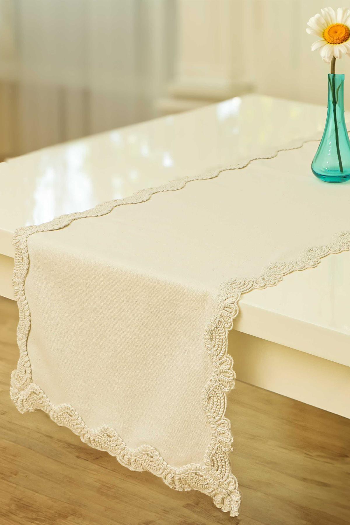 Cremefarbener Tischläufer mit Spitzenbordüre, dekorative und elegante Tischdecke auf einem weißen Tisch