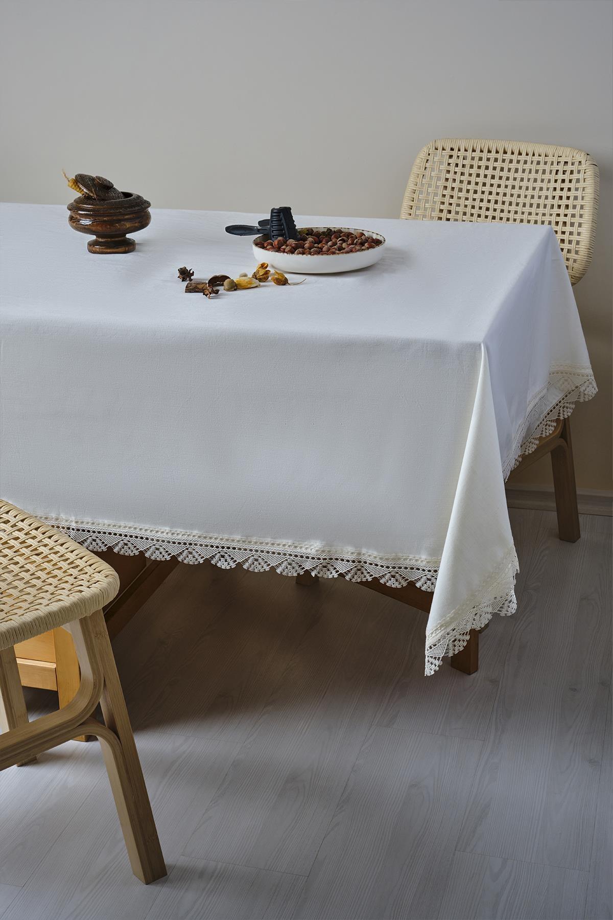 Weiße, fleckabweisende Tischdecke mit Spitze auf einem Tisch mit modernen Holzstühlen.